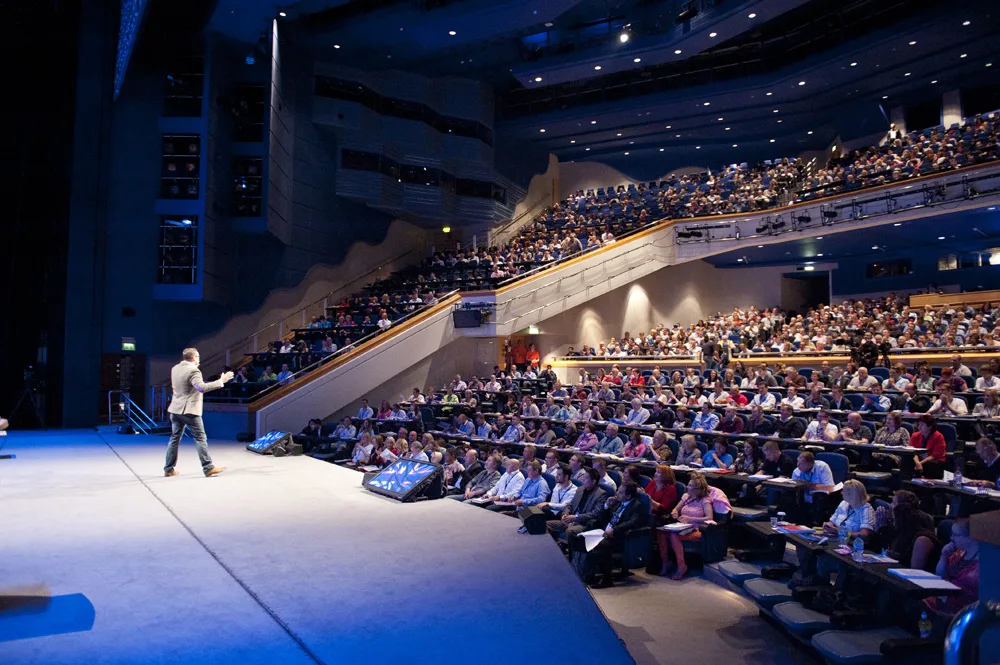 Paul on stage in front of a packed, tiered auditorium.